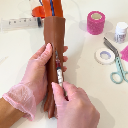 IV Canine Leg Training Kit with a realistic dog leg training arm, blood bag, syringe, bandages, and small medical accessories on a pink background with the text 'IV Canine Leg Training Kit' and 'VET NURSE SCHOOL'.